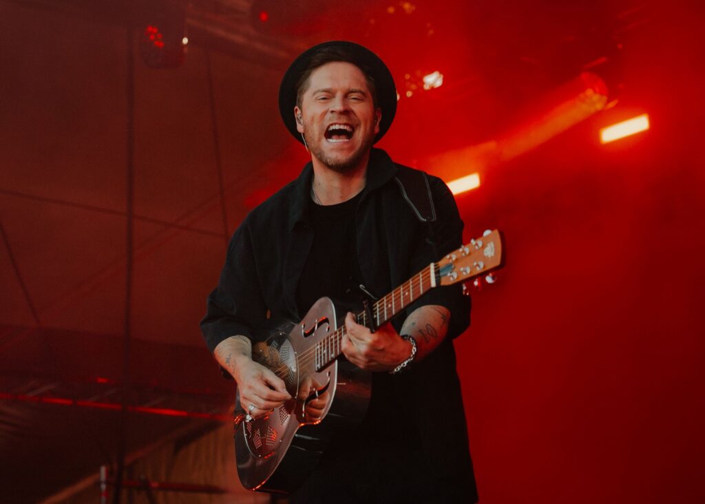 Bühnenfoto von Johannes Oerding beim Singen mit Gitarre im roten Scheinwerferlicht